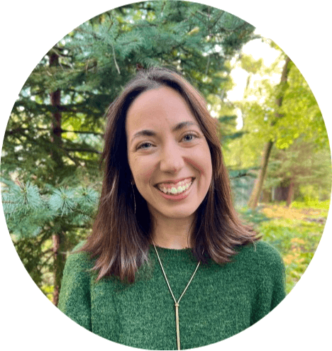 Picture of Laura Tait Smiling with pine trees behind her.